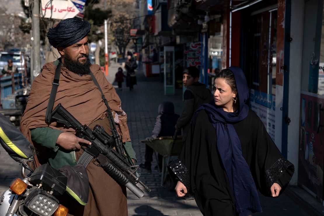 A Taliban fighter stands guard as a woman walks past in Kabul, Afghanistan, on December 26, 2022.